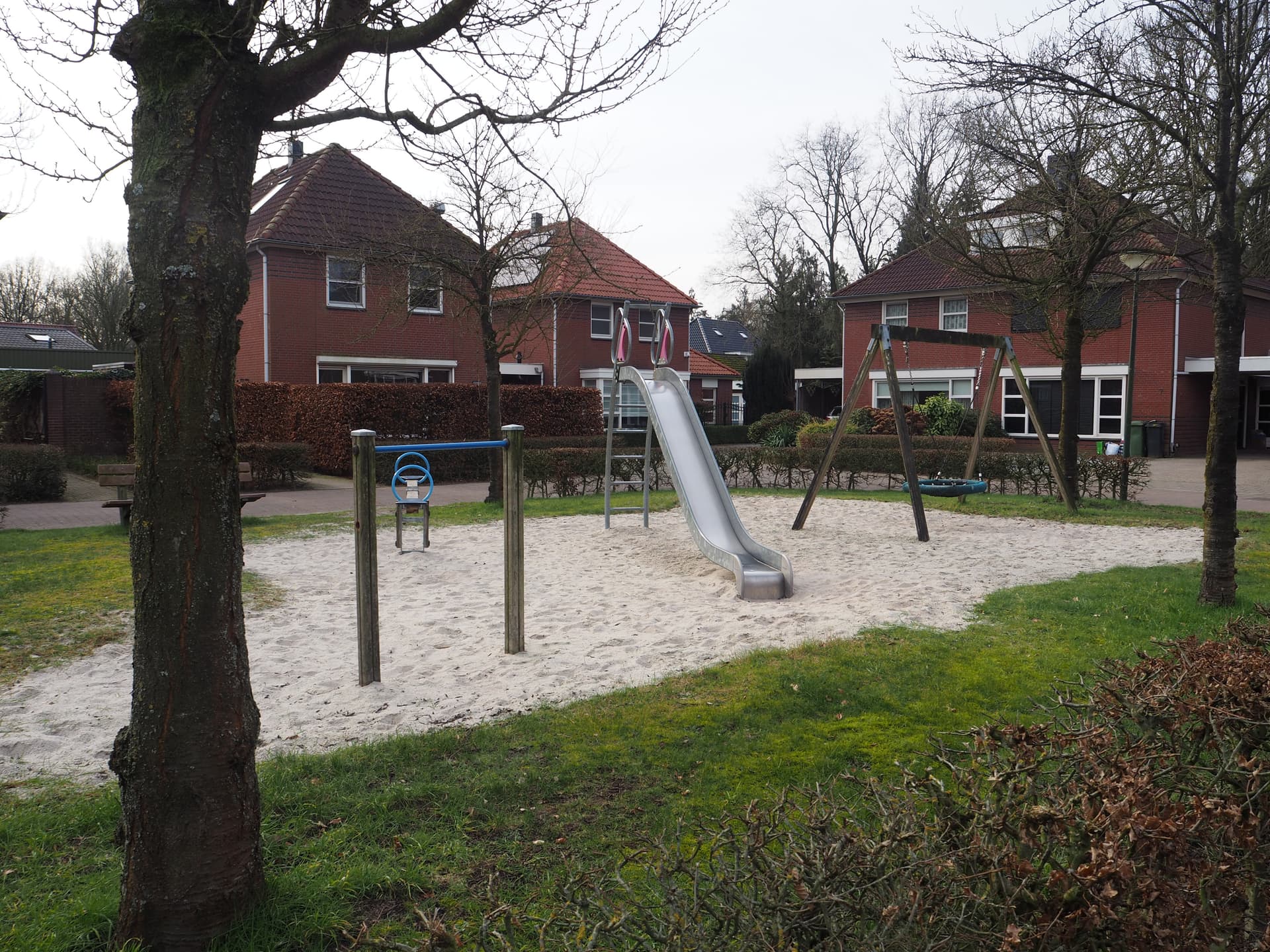 Bild vergrößern: auf der linken Seite ein Purzelbaum und eine Wippe, rechts davon eine Rutsche und daneben eine Schaukel. Im Hintergrund sind Häuser zu sehen.