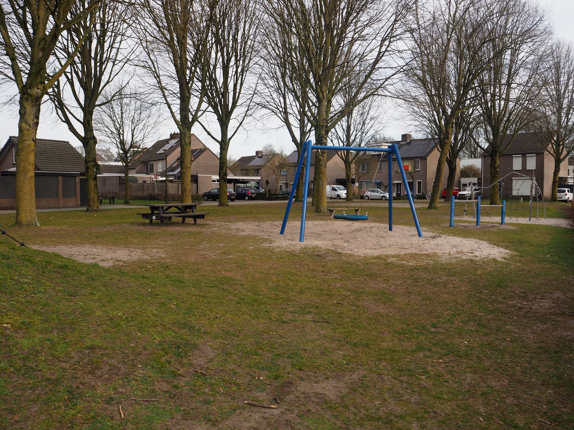 Bild vergrößern: links eine Picknickbank mit einer Schaukel und einem Tummelplatz daneben, im Hintergrund Häuser