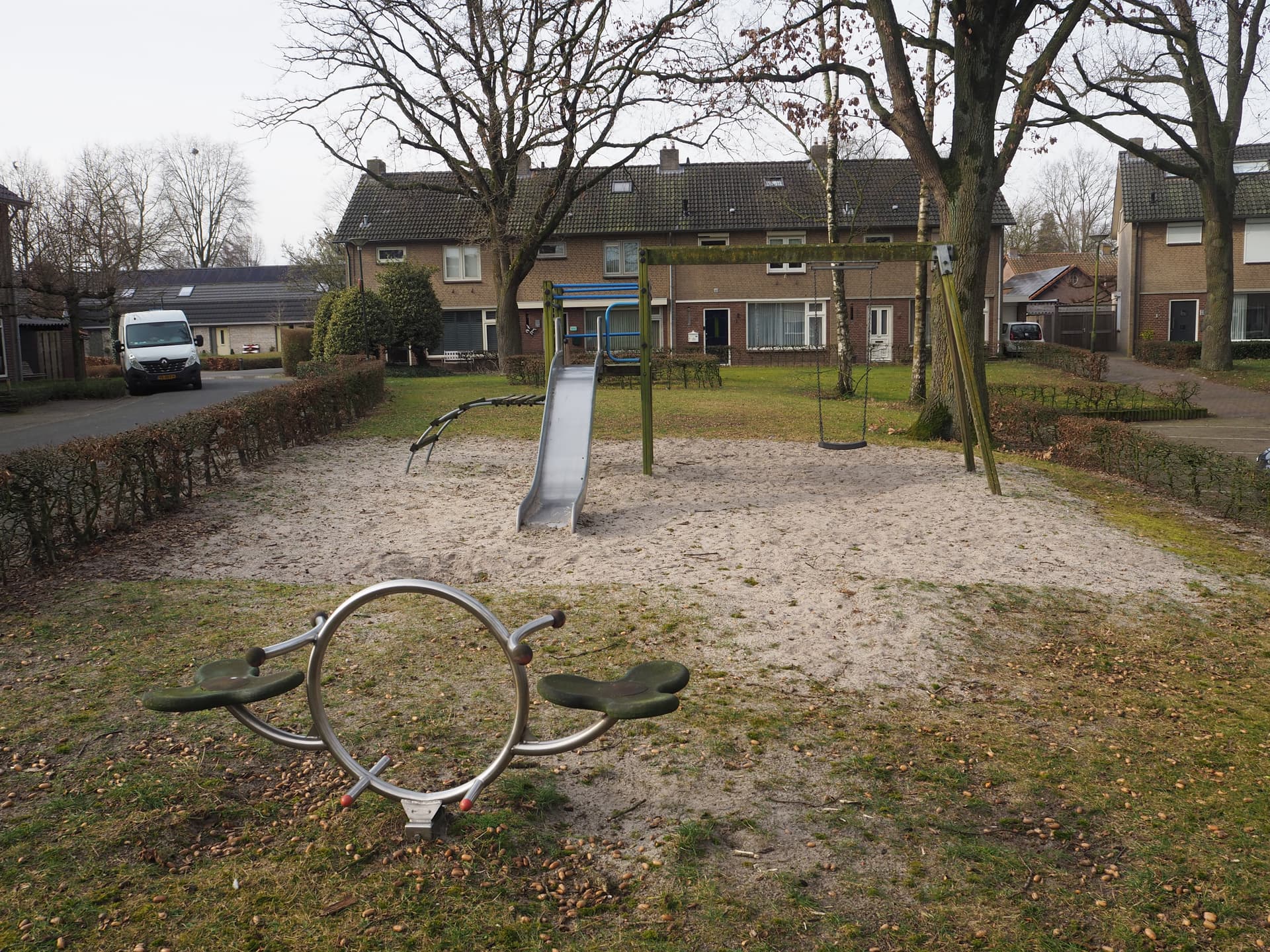 Vergrößerte Darstellung: vorne eine kleine Wippe, dahinter ein Klettergerüst mit Rutsche und Schaukel. Im Hintergrund sind Häuser zu sehen.